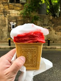 a hand holding an ice cream cone with red and white topping