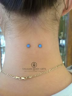 the back of a woman's neck with two small blue stones on her left side