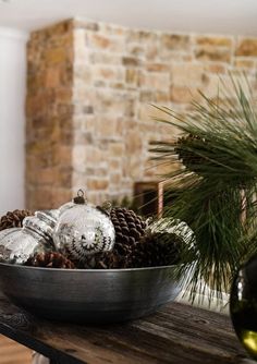 a bowl filled with pine cones on top of a wooden table next to a bottle of wine