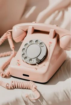 an old pink phone sitting on top of a white bed next to a telephone cord