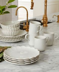 a kitchen counter with white dishes and gold faucets