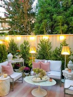 an outdoor living area with white furniture and pink pillows on the floor, surrounded by greenery