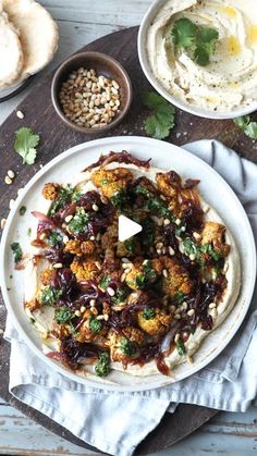 a white plate topped with food next to bowls of hummus and pita bread