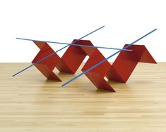 two red sculptures sitting on top of a wooden table next to each other with blue sticks sticking out of them