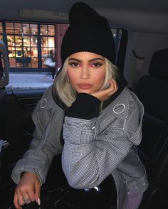 a woman sitting in the back seat of a car wearing a black hat and scarf