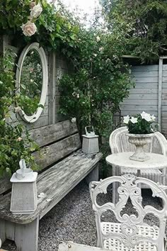 there is a bench, table and chairs in this garden area with roses on the fence