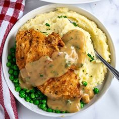 two bowls filled with mashed potatoes covered in gravy next to green peas