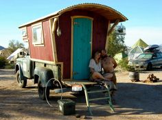 two people sitting on a bench in front of a tiny house