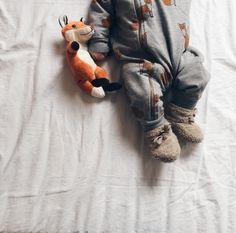 a baby laying on top of a white sheet next to a stuffed animal toy in the shape of a fox