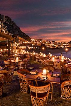 an outdoor dining area with wooden tables and chairs on the beach at night, lit by candles