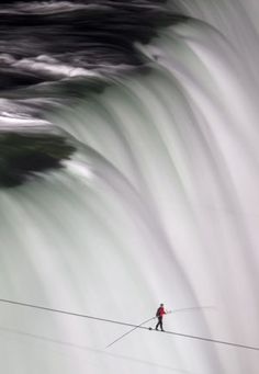 a man walking across a high wire over a river next to a large water fall