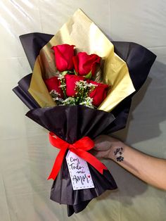 a bouquet of roses wrapped in black paper and tied with red ribbon, held by someone's hand