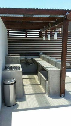 an outdoor kitchen with stainless steel appliances and grilling area in the back yard, under a pergolated roof