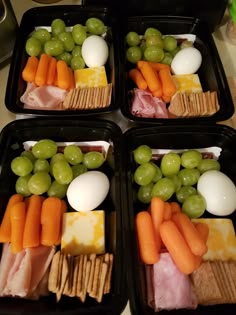 four black trays filled with different types of food including grapes, cheese and crackers