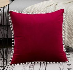 a red pillow with pom - poms on it sitting next to a chair