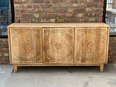 a wooden cabinet with intricate carvings on the front and side panels, in front of a brick wall