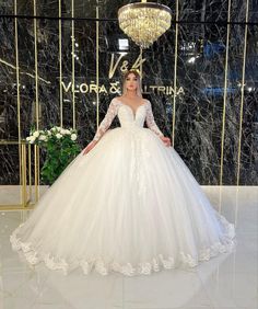 a woman standing in front of a chandelier wearing a wedding dress with long sleeves