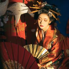 a woman in an orange kimono and crane headdress holding a red fan