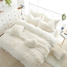 a white bed with fluffy pillows on top of it in a room next to a dresser