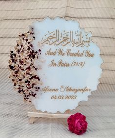 a white plaque sitting on top of a wooden stand next to a red rose in front of a striped wall