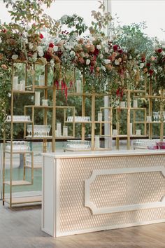 a white and gold reception table with flowers hanging from it's sides, surrounded by greenery