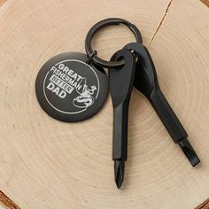 a pair of black scissors sitting on top of a piece of wood next to a keychain