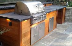 an outdoor kitchen with grills and lights on the counter top in front of it