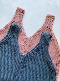 two knitted vests sitting next to each other on top of a white surface