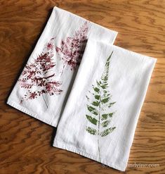 two white towels with red and green leaves on them sitting on a wooden table next to each other