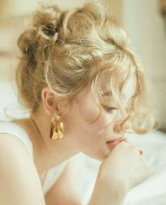 a woman laying on top of a bed next to a white pillow and wearing gold earrings