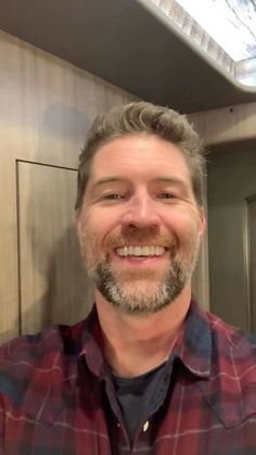 a man with grey hair and beard wearing a red plaid shirt smiles at the camera