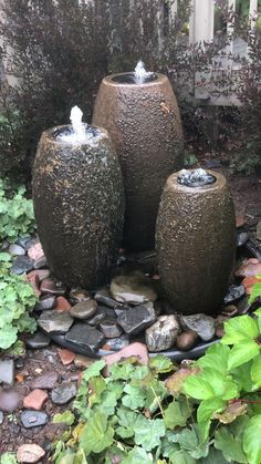 three water fountains are in the middle of a garden area with rocks and plants around them