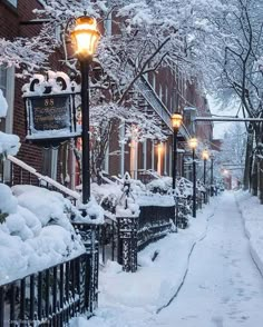 a snowy street lined with buildings and lamps on the side of each building is covered in snow