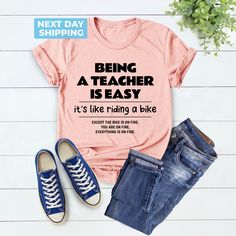 Cute Teacher Shirt, Being A Teacher Is Easy Back To School Like Riding A Bike, School Shirt, Funny Teacher Shirt, Unique Gift, Teacher Gift Hi! Welcome to the LaTeeApparel!  It's great to see you here! Our shirts are clean, high quality and soft. It is prepared quickly by our store! Enjoy your shopping! It is a pleasure for us to help you with your questions and you can reach us at any time. F I T  ∙ S I Z I N G  -->Women's sizes are narrower than the waist -->Sleeves are rolled up in some produ Short Sleeve Graphic Print Cycling Tops, Graphic Print Short Sleeve Cycling Top, Graphic Print Short Sleeve Tops For Cycling, Casual Cotton T-shirt For Cycling, Being A Teacher, Riding A Bike, Teacher Things, Funny Teacher, Gift Teacher