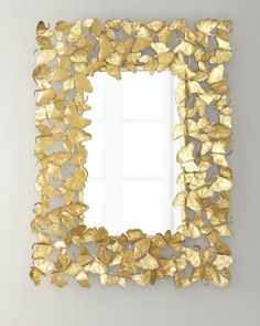 a mirror that is on the wall with gold leaves in front of it and a vase next to it