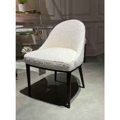 a white chair sitting on top of a floor next to a glass table and vase