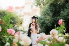 a woman wearing a graduation cap and gown standing next to a man in front of flowers