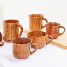 six wooden coffee mugs sitting on top of a table next to a cutting board