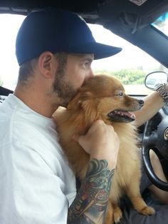 a man sitting in the driver's seat of a car with his dog on his lap