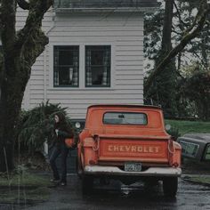 an old chevrolet truck parked in front of a house with a woman standing next to it