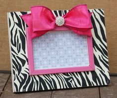 a zebra print frame with a pink bow and diamond brooch on the top, sitting on a wooden floor