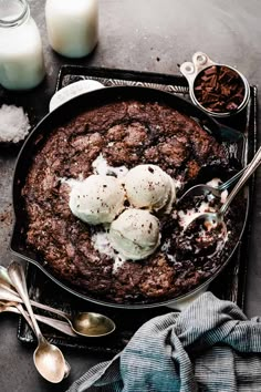 a chocolate dessert with ice cream on top and spoons next to it, along with two glasses of milk