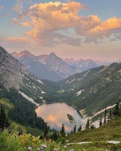 a lake in the middle of a mountain range with mountains in the background and clouds above it