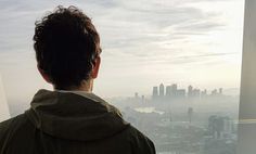 a man standing in front of a window looking out at a cityscape and skyscrapers