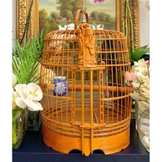 a bird cage sitting on top of a table next to some flowers and vases