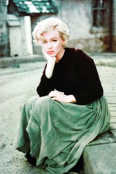 a woman sitting on top of a cement block in front of a brick building and looking at the camera