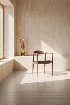 a wooden chair sitting in the middle of a room next to a vase with flowers