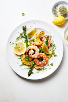 a white plate topped with shrimp and asparagus next to lemon wedged bread