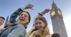 two women and a man standing in front of a clock tower with their arms up