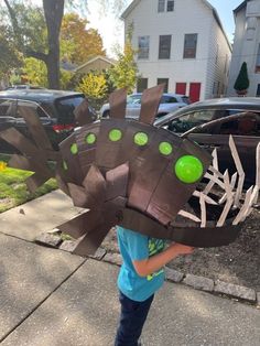 a young boy is holding up a paper plate shaped like a dinosaur's head